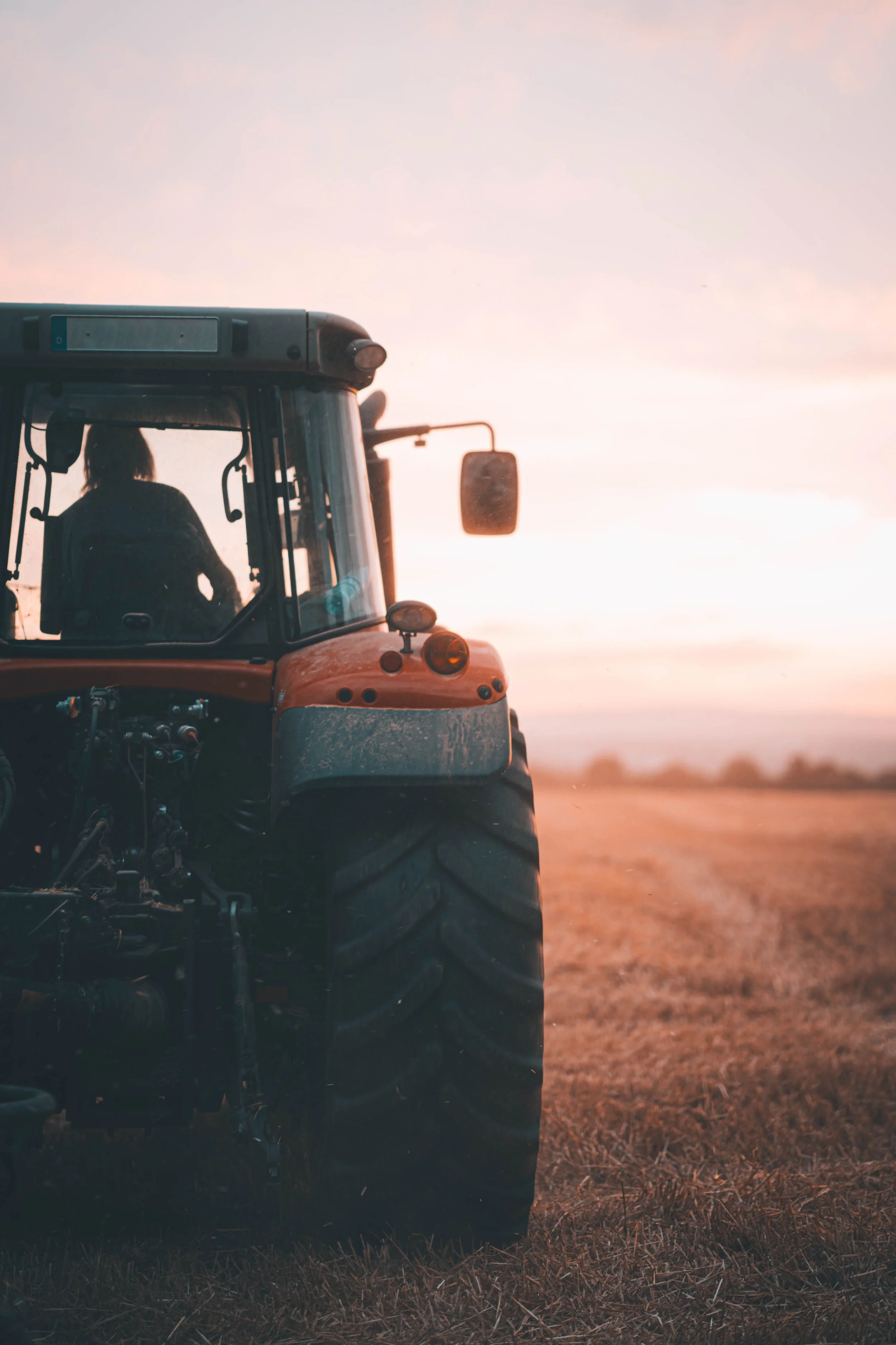 A tractor on a farm during sunset with a person visible inside the cab.