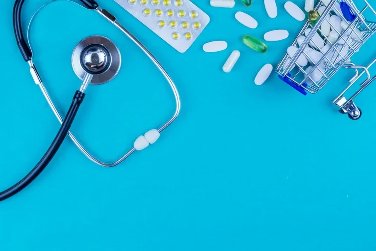 Medical stethoscope, blister pills, capsules, and a miniature shopping cart on a blue background