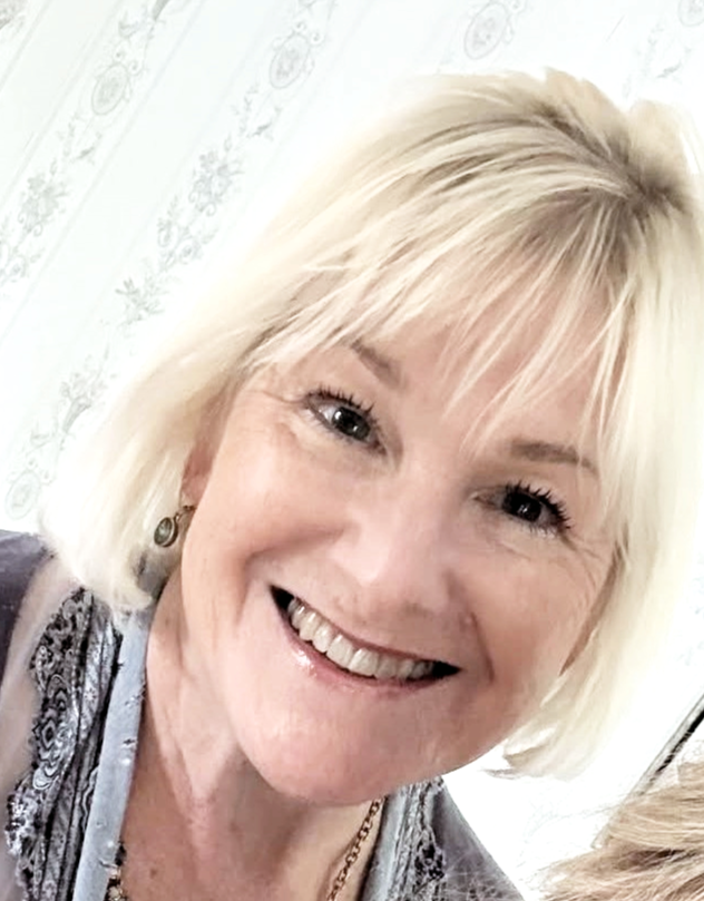 A woman with blonde hair smiling in front of a white patterned background.