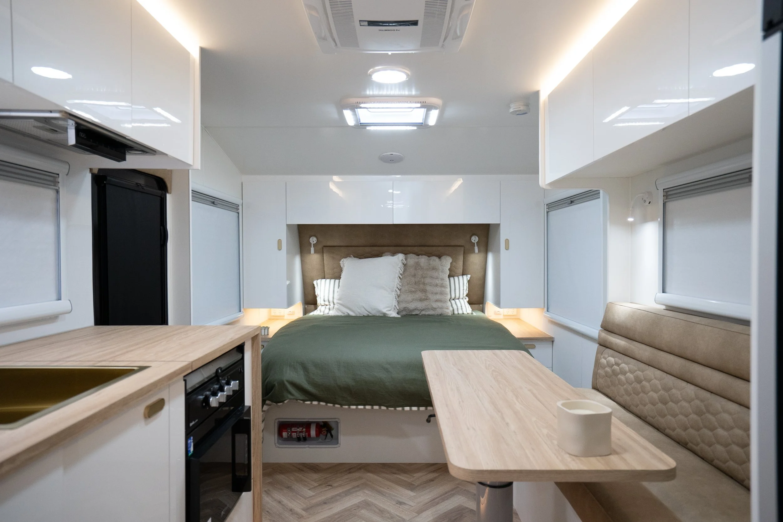 Bespoke Caravans Family Summit 23 foot bunk caravan interior showing kitchen, L-lounge and queen size bed with sleek white overhead storage throughout and beautiful neutral toned furniture and benchtops