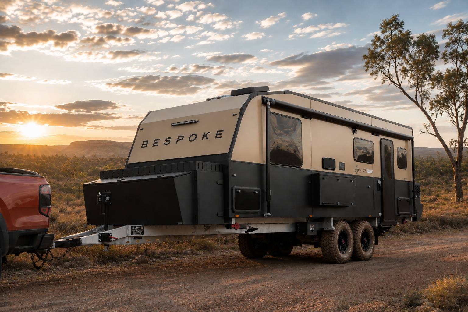 Luxury Australian Off-Road Caravan titled "Bespoke" at the front of the van with an Australian sunset in the background on a dirt road. The caravan is 22' with modern smooth black plates and scenery reflecting off of the tinted windows.