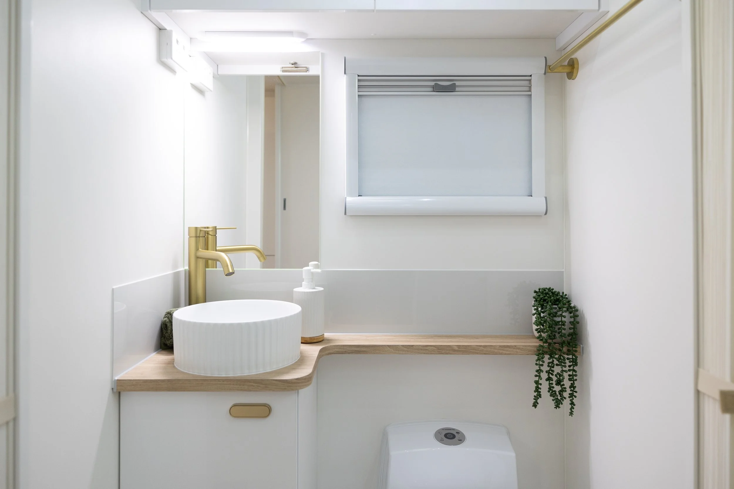Bespoke Caravans 23 foot Family Summit bunk van interior photo showing beautiful light feeling full ensuite bathroom with window, mirror, neutral wood toned bench top, luxury ripple-textured ceramic basin and gold tapware.
