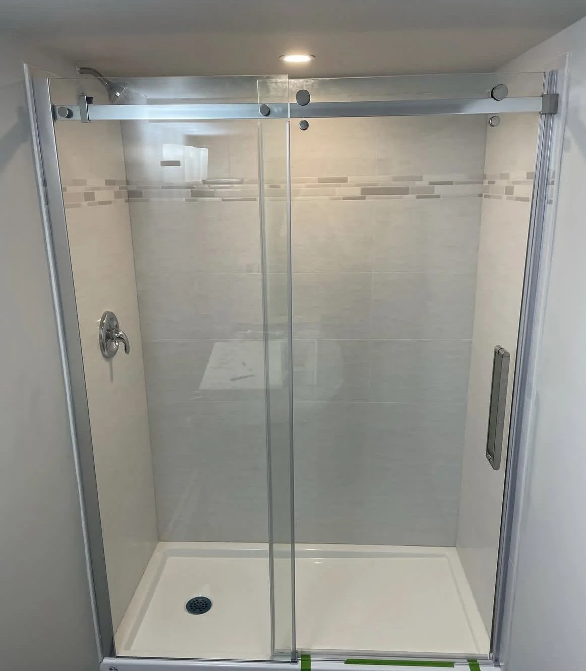 Empty glass shower enclosure with sliding doors, showerhead on the left wall, and tiled walls inside.