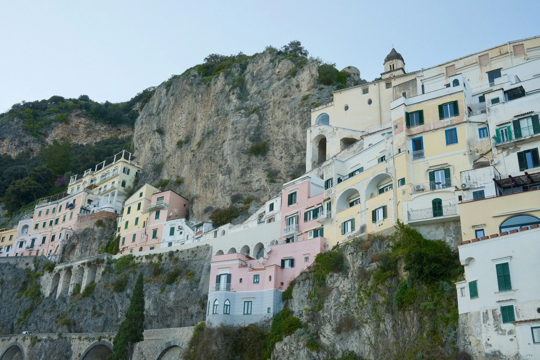 Colorful buildings built into a steep hillside with a large rocky cliff and greenery behind them.