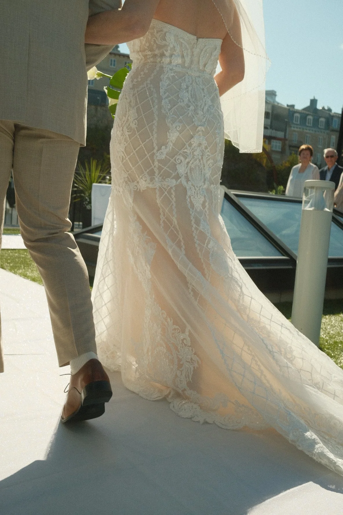 Bride in a lace wedding dress and groom in a beige suit at an outdoor wedding ceremony.