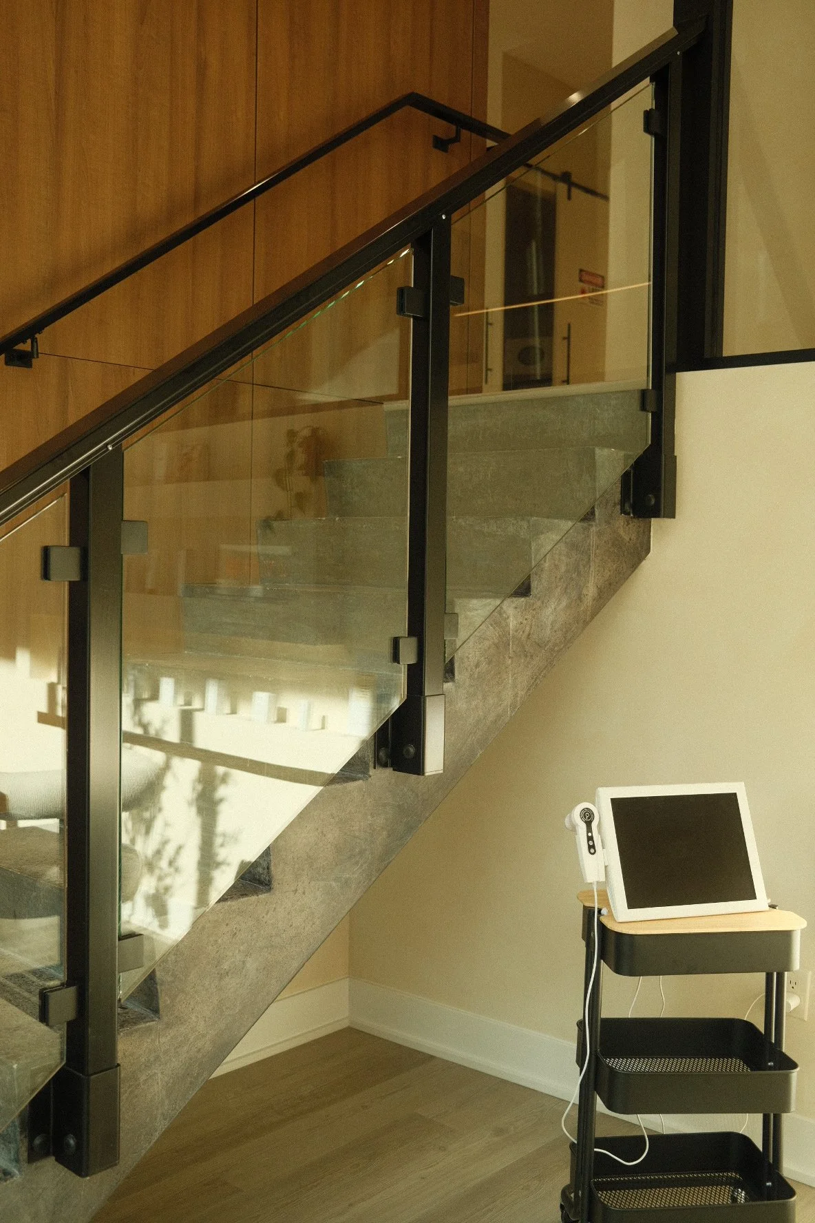 Indoor staircase with glass railing, wooden wall, and a small table with a monitor and a device on it.