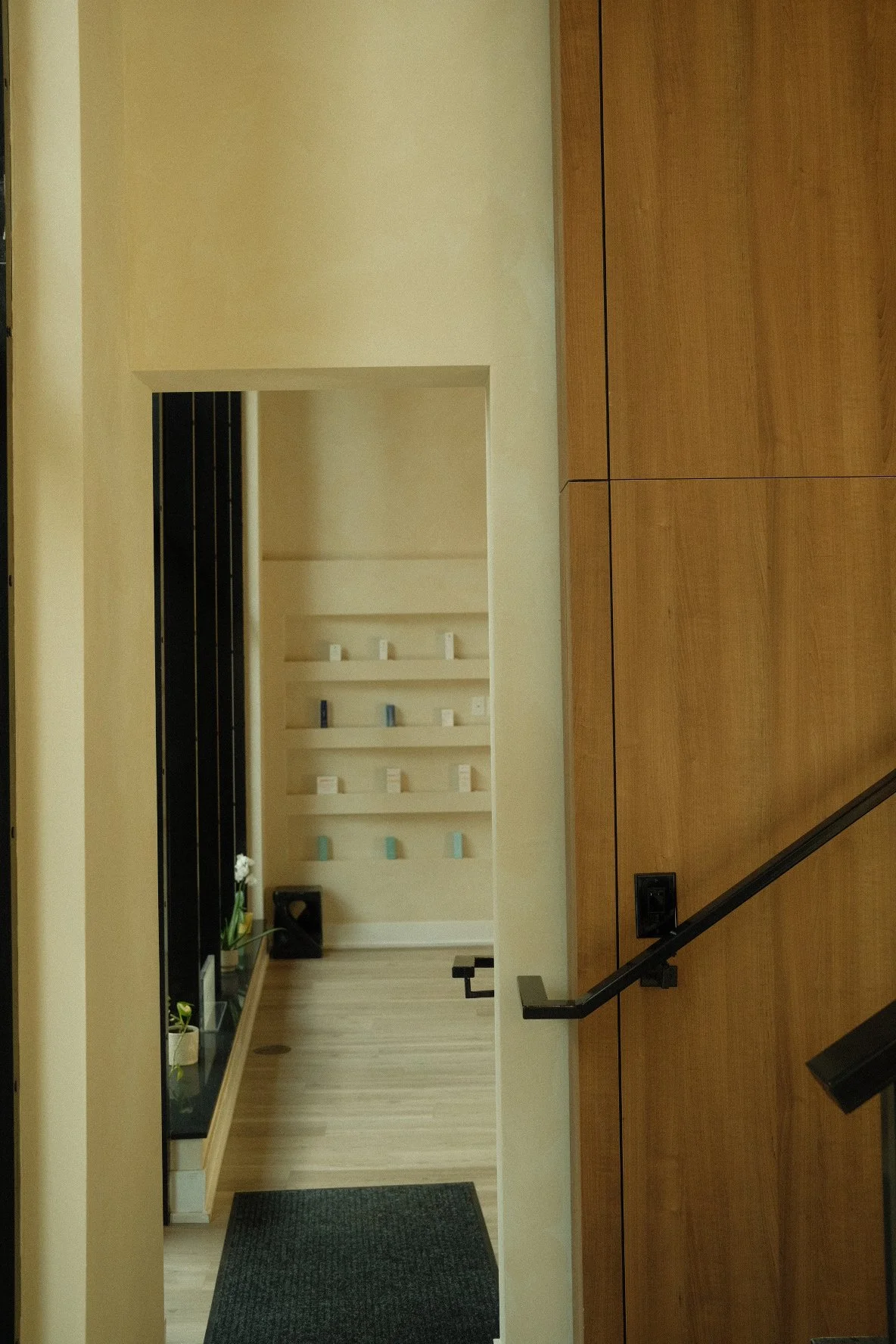 Interior view of a hallway with a staircase, wooden wall panels, a built-in shelf with decorative items, and a small plant on the floor.