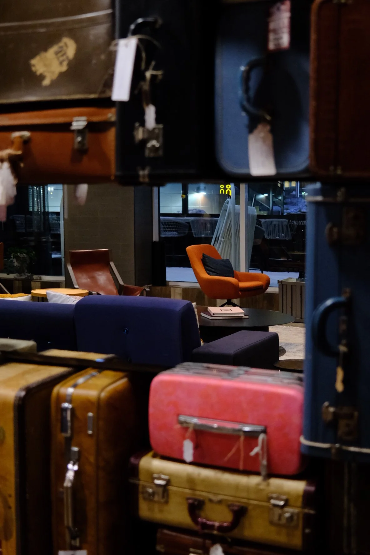 A cozy indoor seating area with colorful chairs, a black coffee table, and a beige rug, viewed through a luggage cart with suitcases in the foreground.