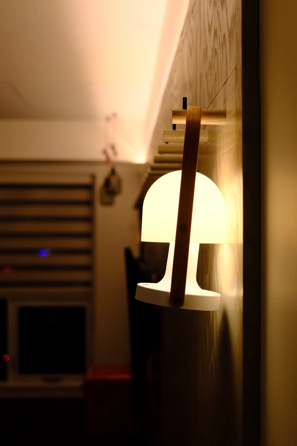 A modern wall-mounted lamp with a curved white shade and a wooden support, illuminating a room with warm light.