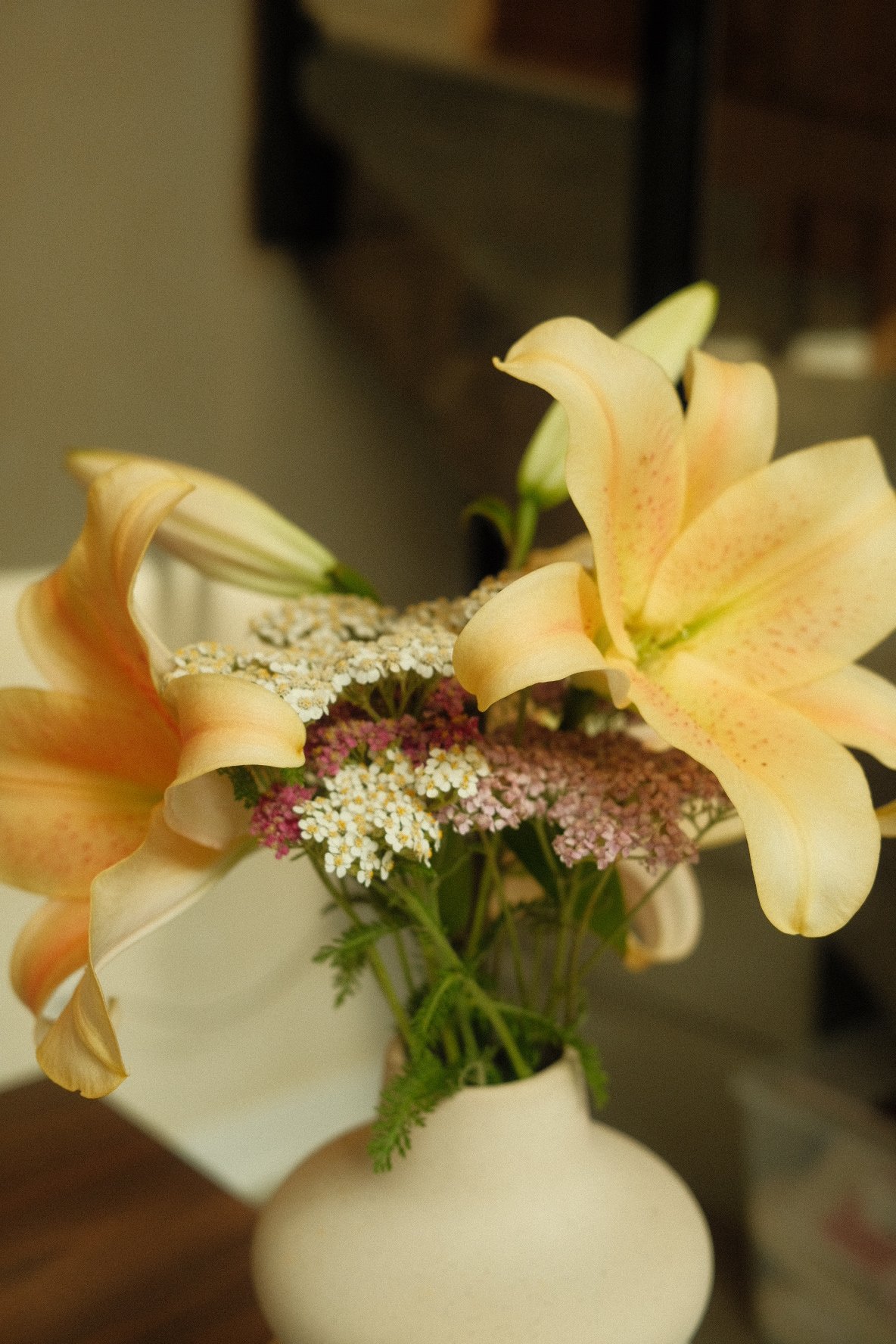 A bouquet of yellow lilies with small white and pink filler flowers in a white vase.