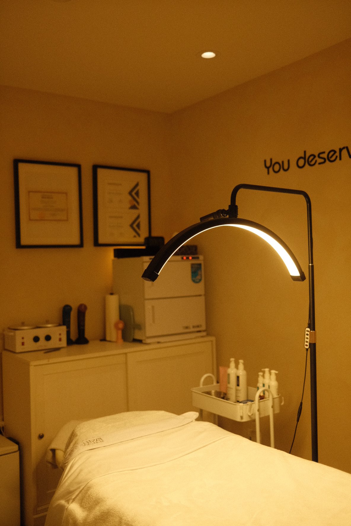 A dimly lit hospital room with a bed, medical equipment, and a modern lamp overhead.