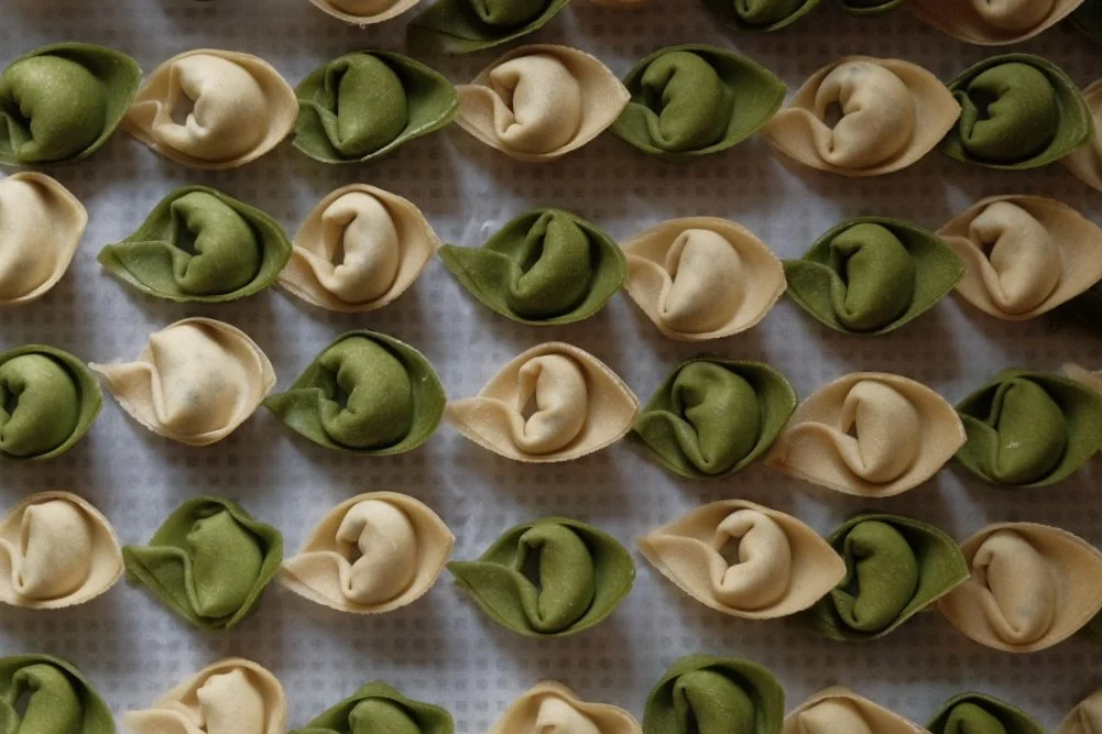 Uncooked tortellini pasta in green and beige colors arranged on a baking sheet lined with parchment paper.