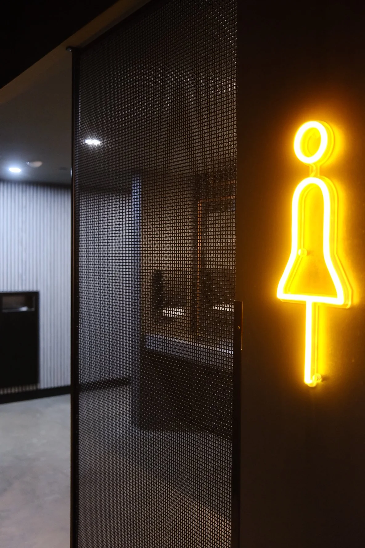 Bright yellow neon sign of a female figure on a black wall in a modern interior.
