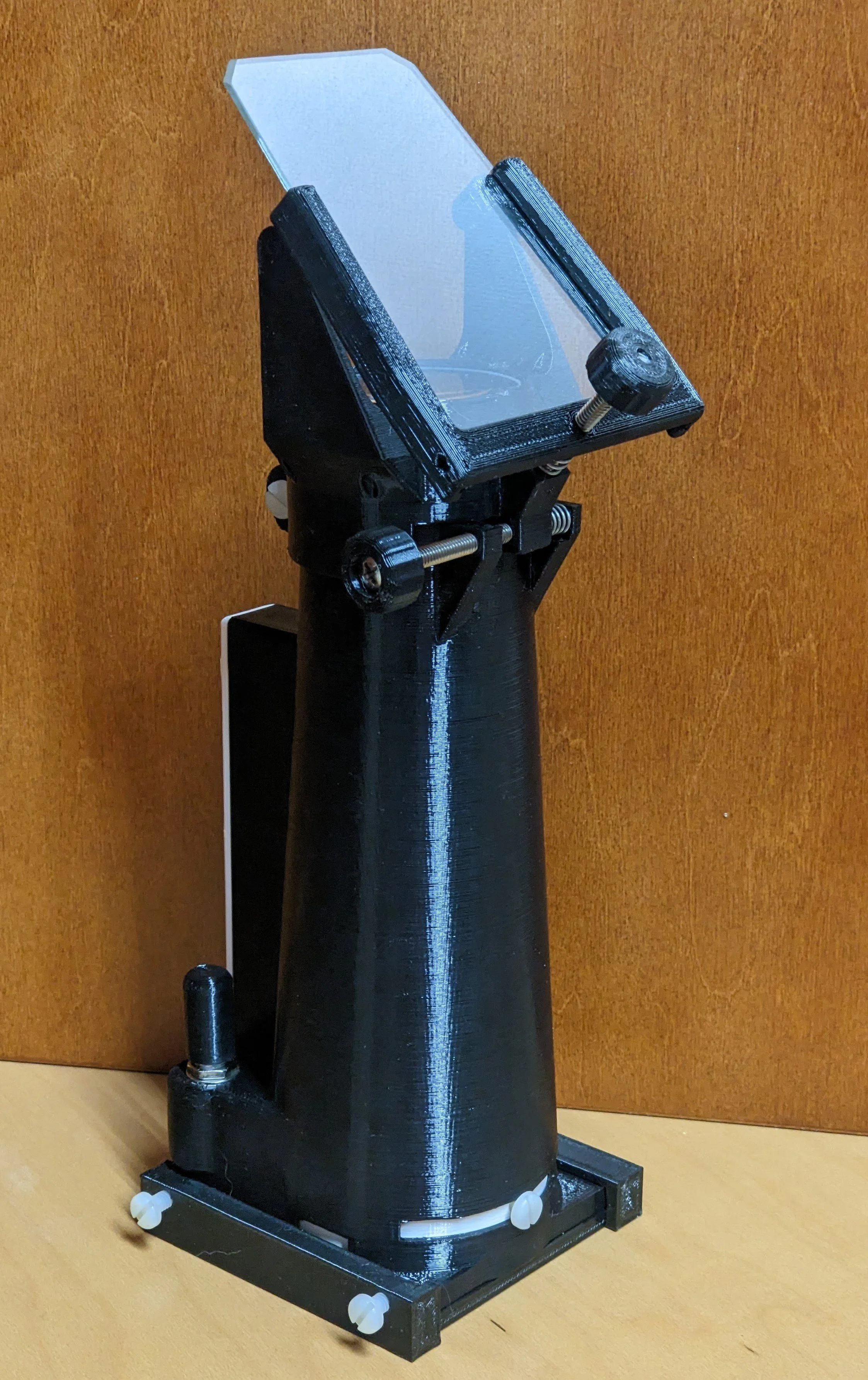 A black, cylindrical scientific device with a transparent top, mounted on a black base with white knobs, set against a wooden background.