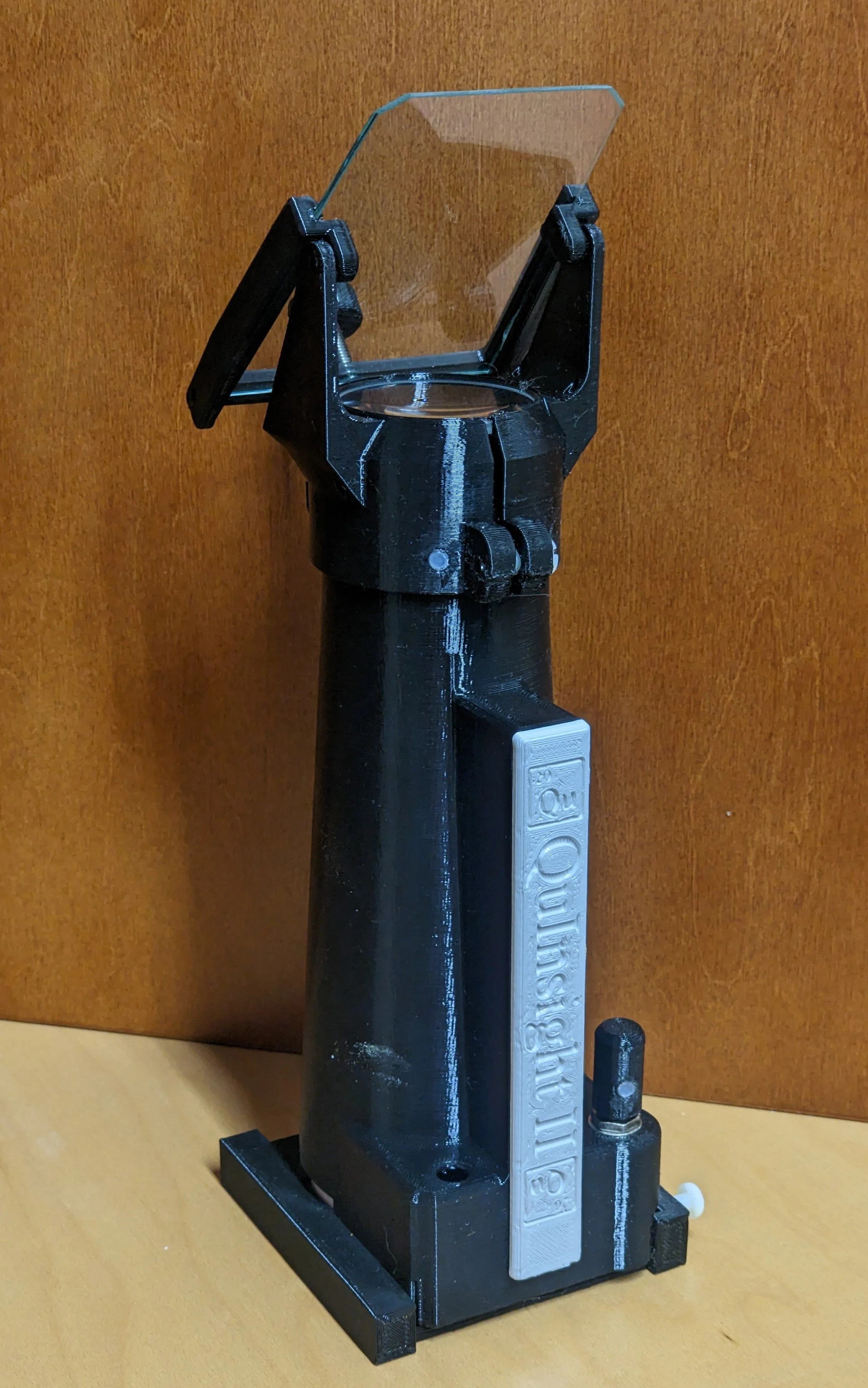 A 3D-printed black plastic device with a clear plastic shield at the top, mounted on a black stand with a white component labeled 'Polymer Science'.
