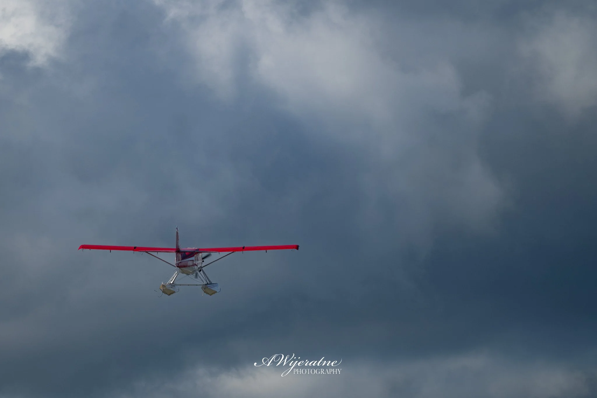 A small red and white seaplane flying through a cloudy sky.