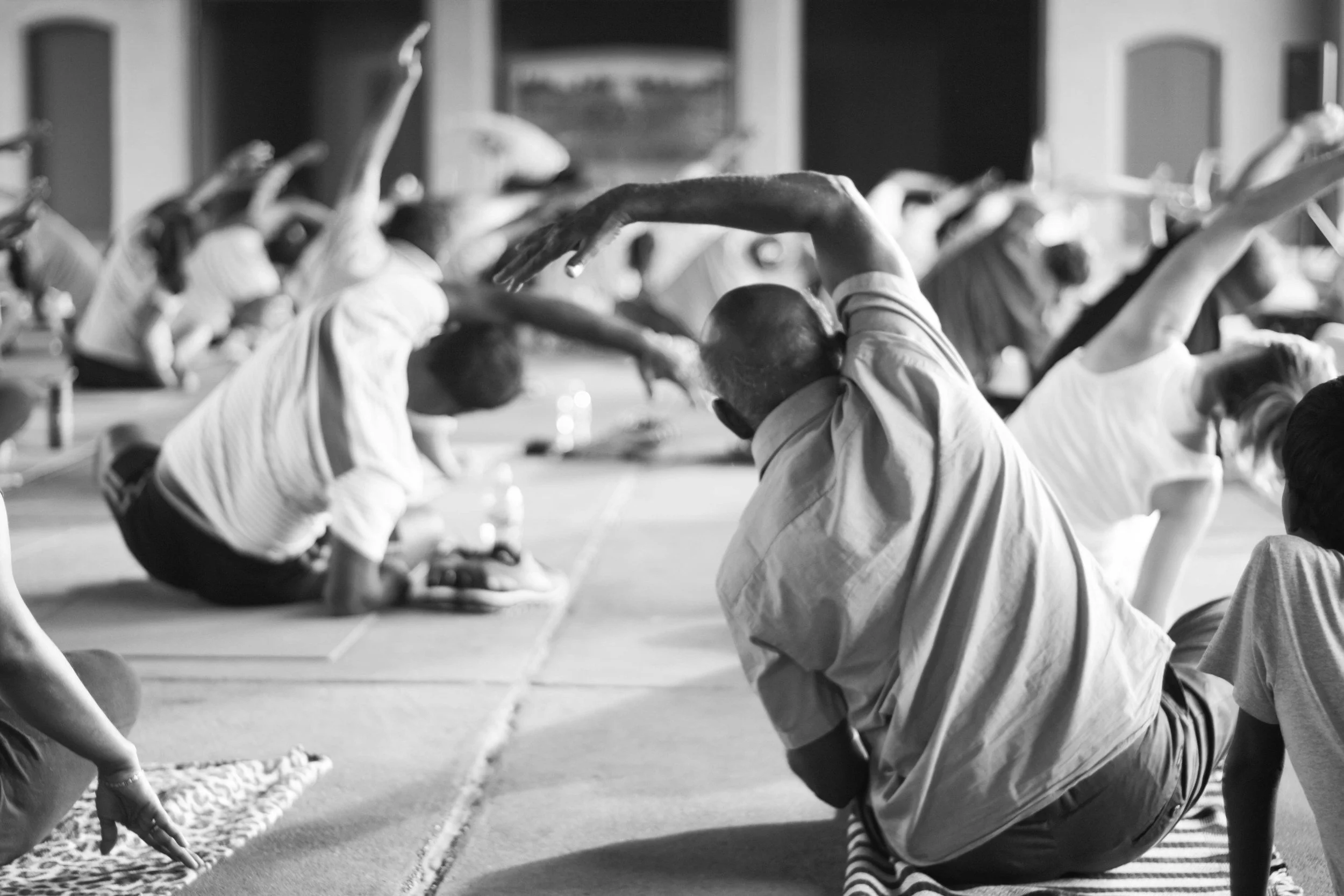 A group of people practicing yoga or meditation indoors, sitting cross-legged with their arms raised overhead in a peaceful pose.