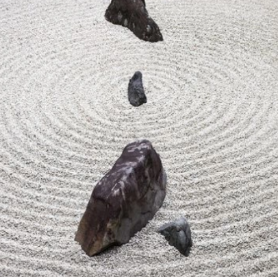 Five rocks arranged on a Japanese zen garden sand with circular ripple patterns.