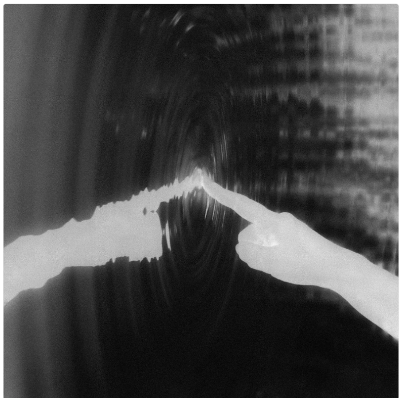 Two hands touching inside a dark, swirling tunnel, with one hand illuminated and the other darker.
