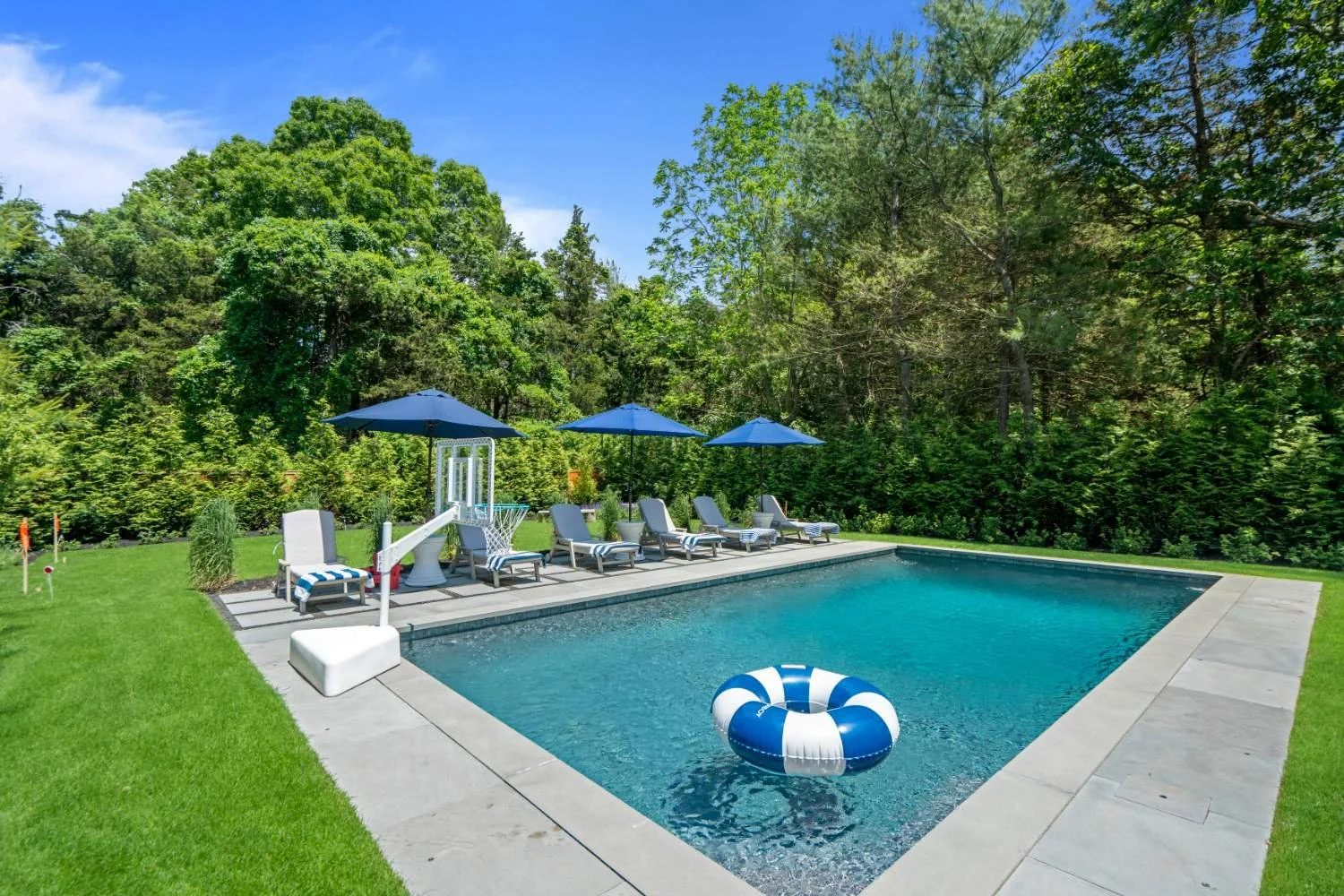 outdoor swimming pool surrounded by green grass and trees with lounge chairs, umbrellas, and a float in the pool