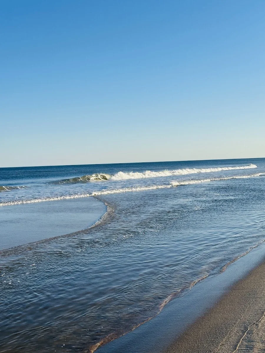 Clear blue sky over a calm ocean with gentle waves hitting the sandy beach.