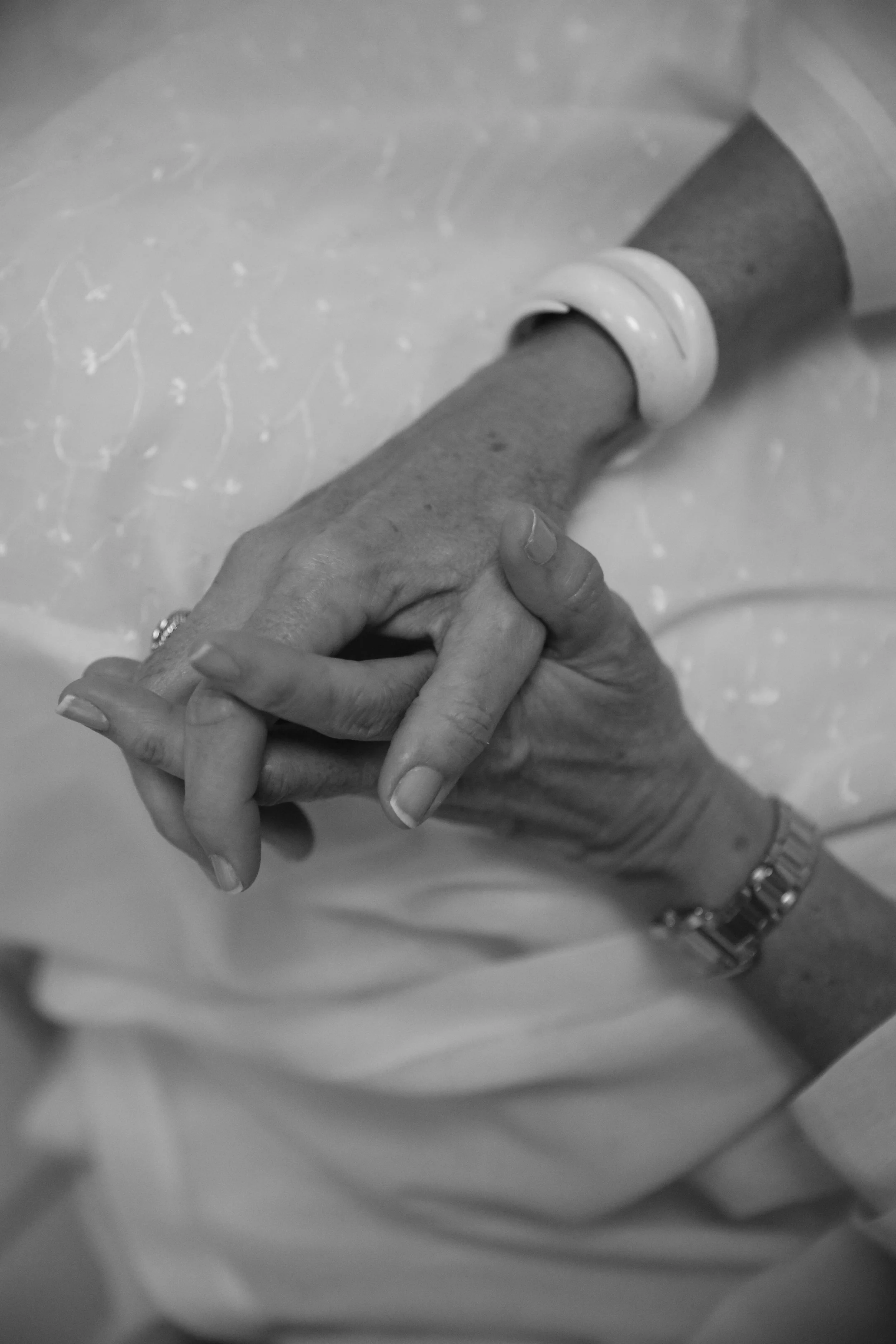 Close-up of a person's hand with a ring, holding another person's hand with a ring, against a blurred background.