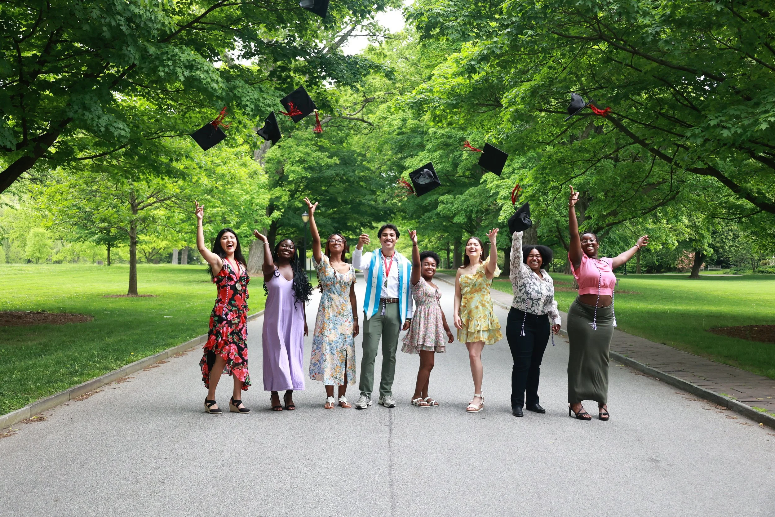 A group of diverse graduates celebrating outdoors in a park, tossing their graduation caps into the air."}