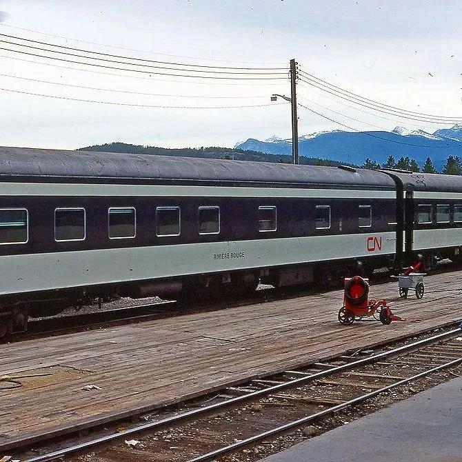 A train called Riviere Rouge on tracks with mountains and cloudy sky in the background. 