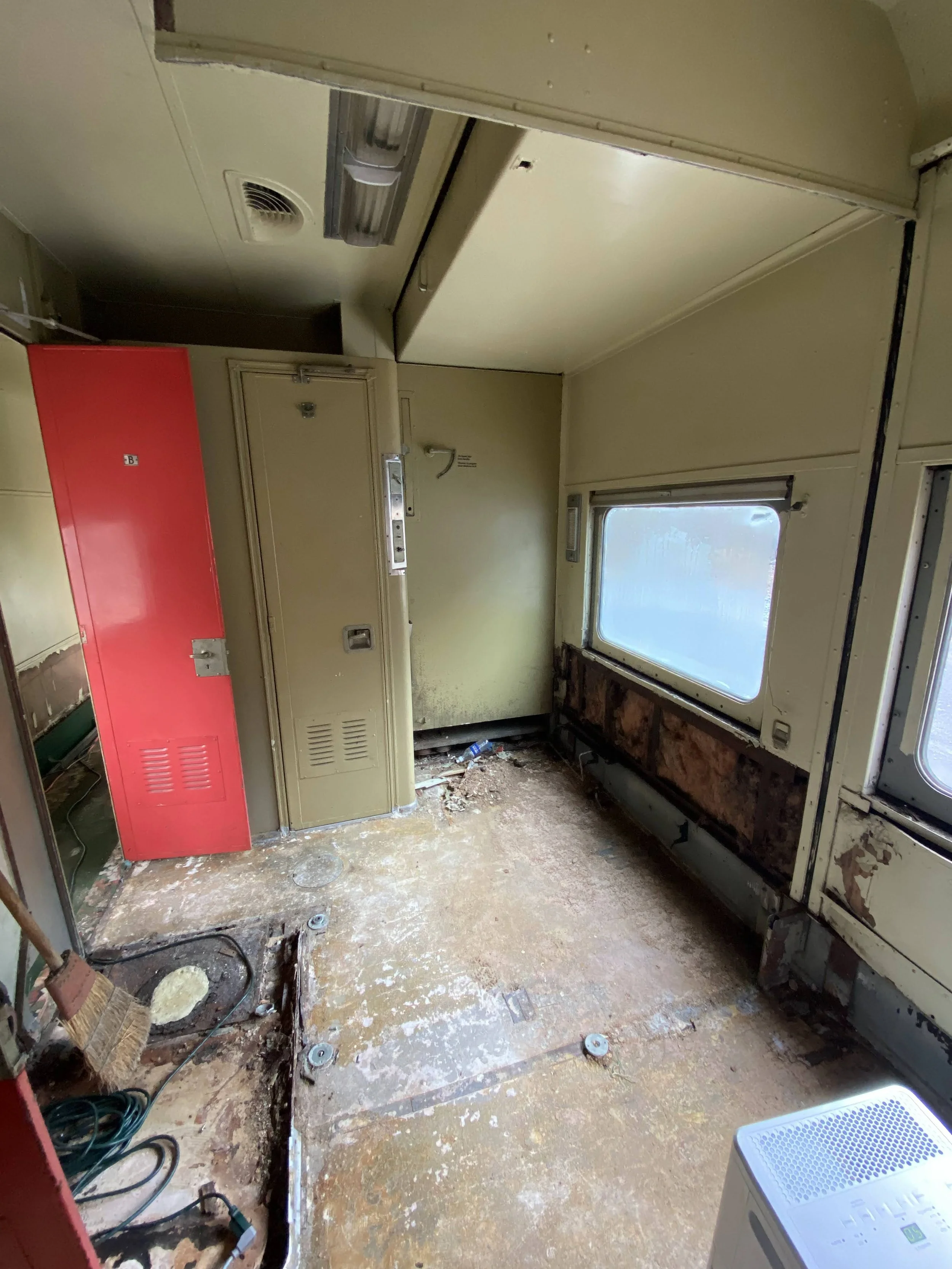An bedroom in the train with stripped walls, exposed floorboards, and an old window before it is renovated. 