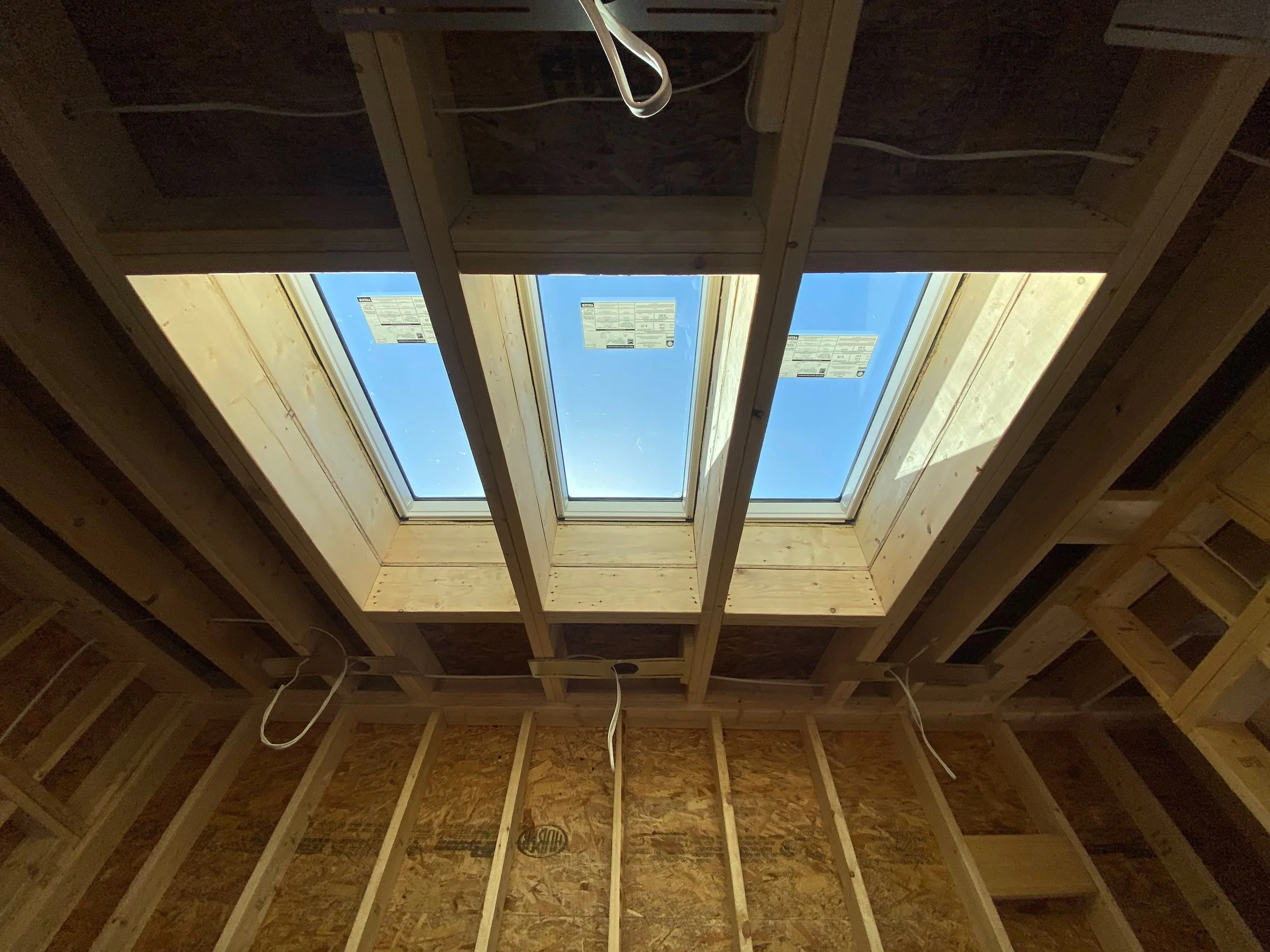 Interior view of a building under construction, showing wooden framing and a large skylight window installed in the ceiling.