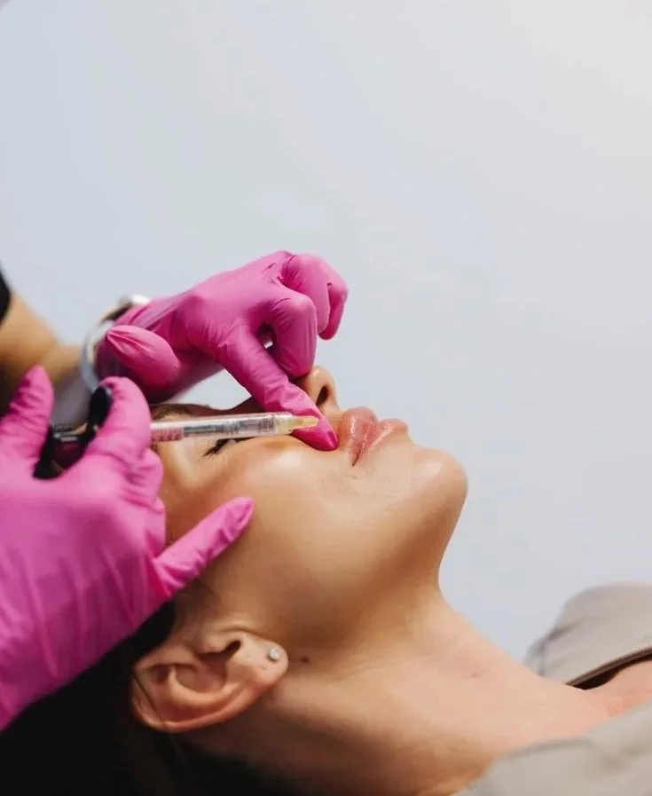 A woman receiving a cosmetic injections in her lips from a professional wearing pink gloves.