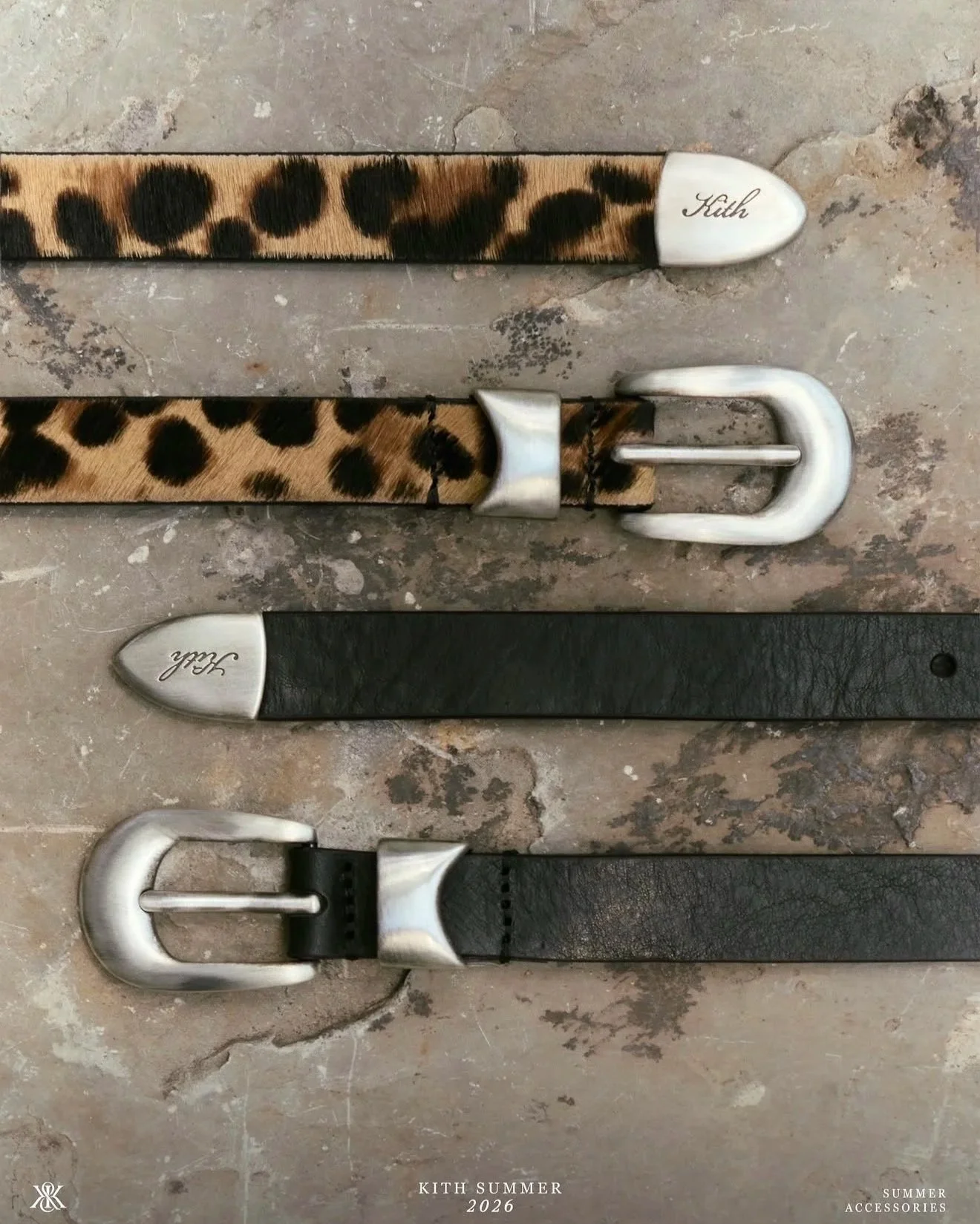 A flat lay of four belts with animal print and metallic buckles on a textured stone surface. The belts feature leopard and black designs, with one embossed with the brand name 'Kith' and another with 'Subh'.