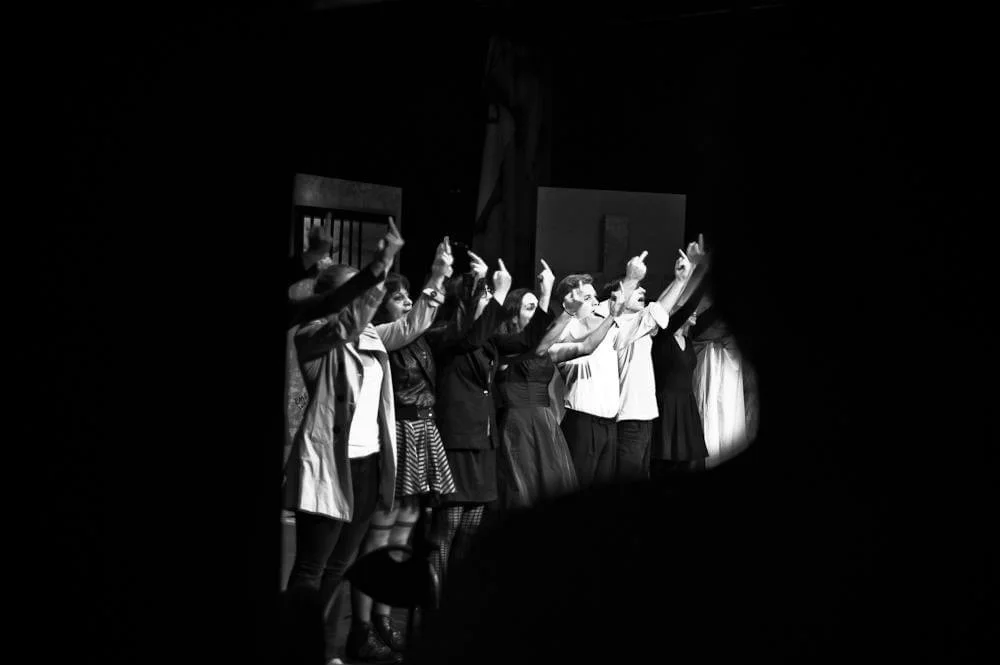 A group of people on stage taking a bow after a performance, visible through a small opening in the dark.