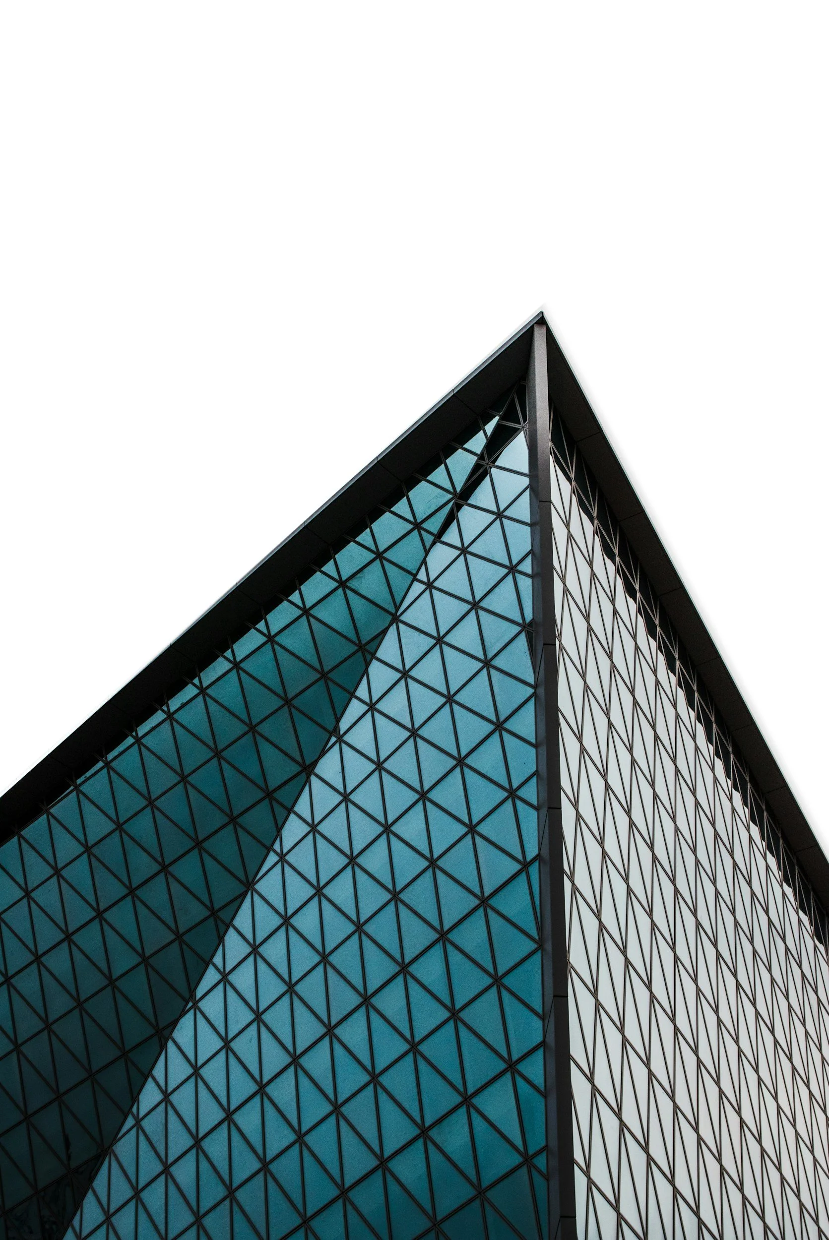 Close-up view of modern glass office building with triangular patterns on the facade, taken from a low angle against a white sky.