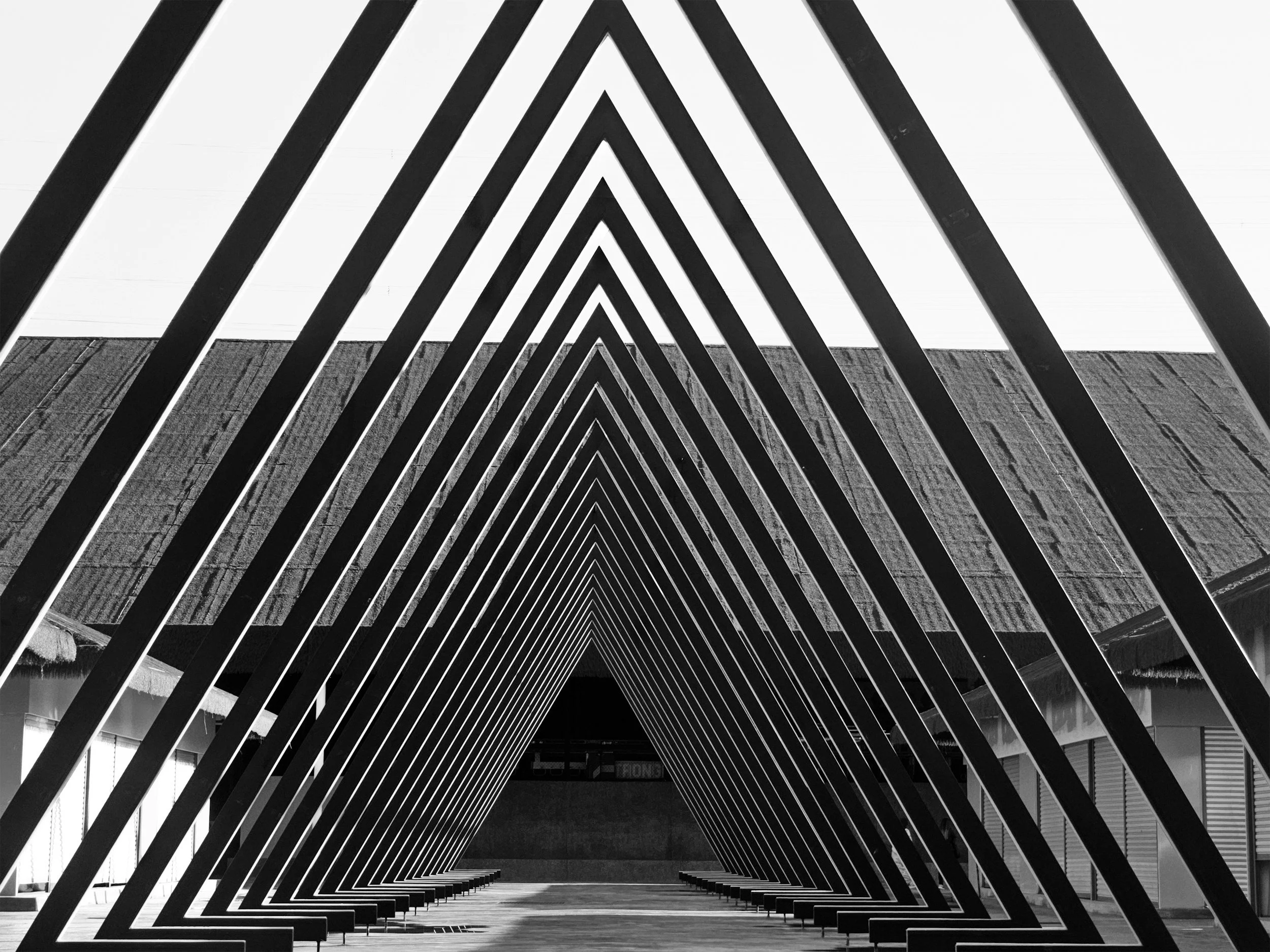 A black and white photo of a modern architectural structure with diagonal beams forming triangular patterns over a corridor or open space within a building.