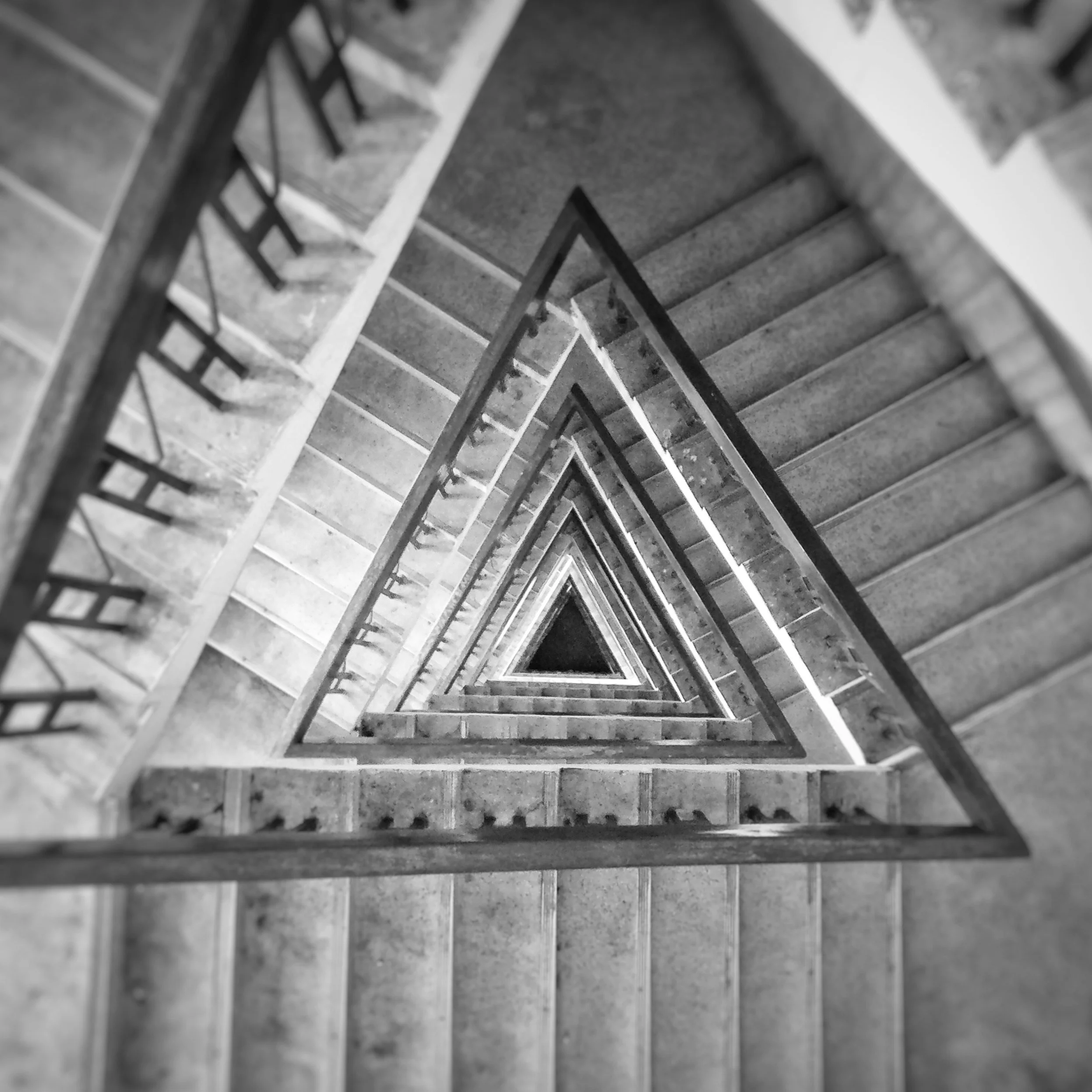 Black and white photo of a downward view of a spiral staircase with metal railings and concrete steps.