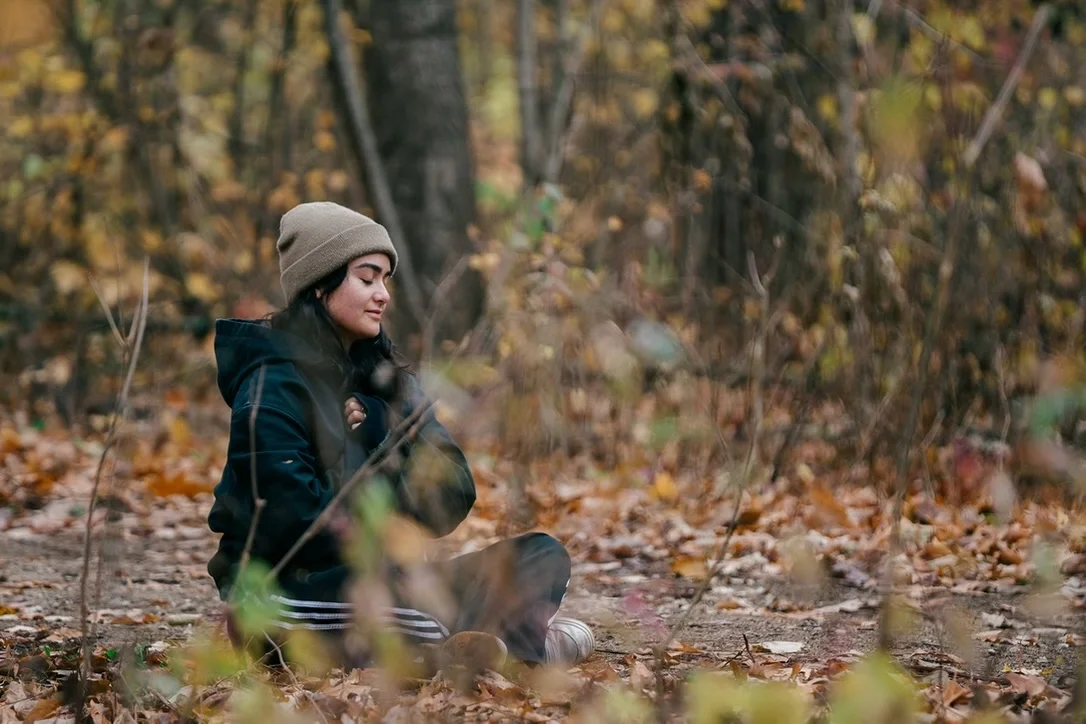 Young woman in a beanie sitting among fallen leaves in an autumn forest