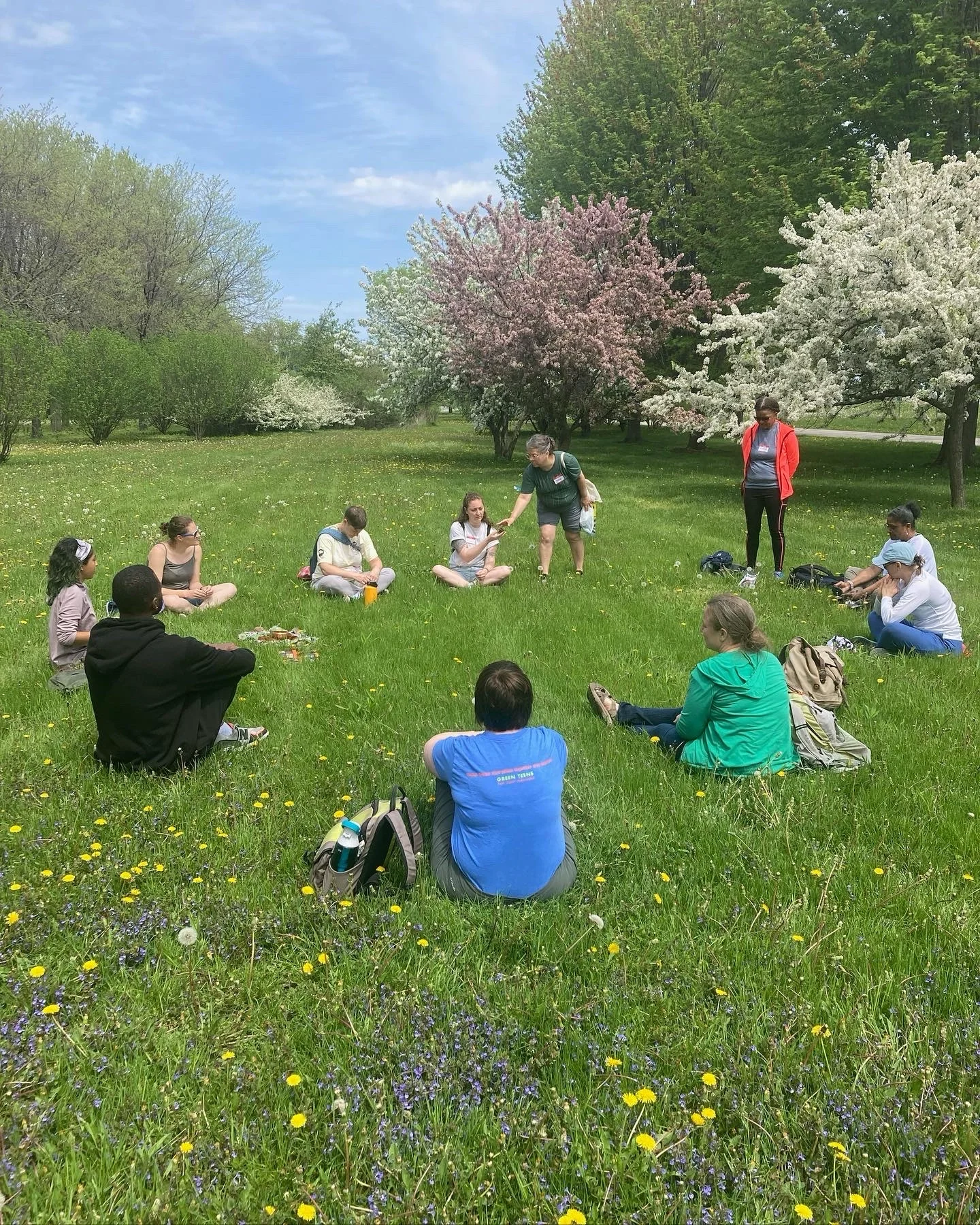 A woman shares a piece of nature with a group sitting in a circle
