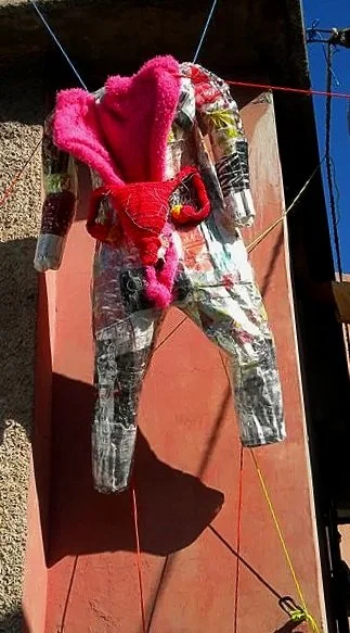 A body suit made of couture shopping bags with a soft pink lining and crocheted reproductive organs exposed strung up in an art yard in port au prince haiti.