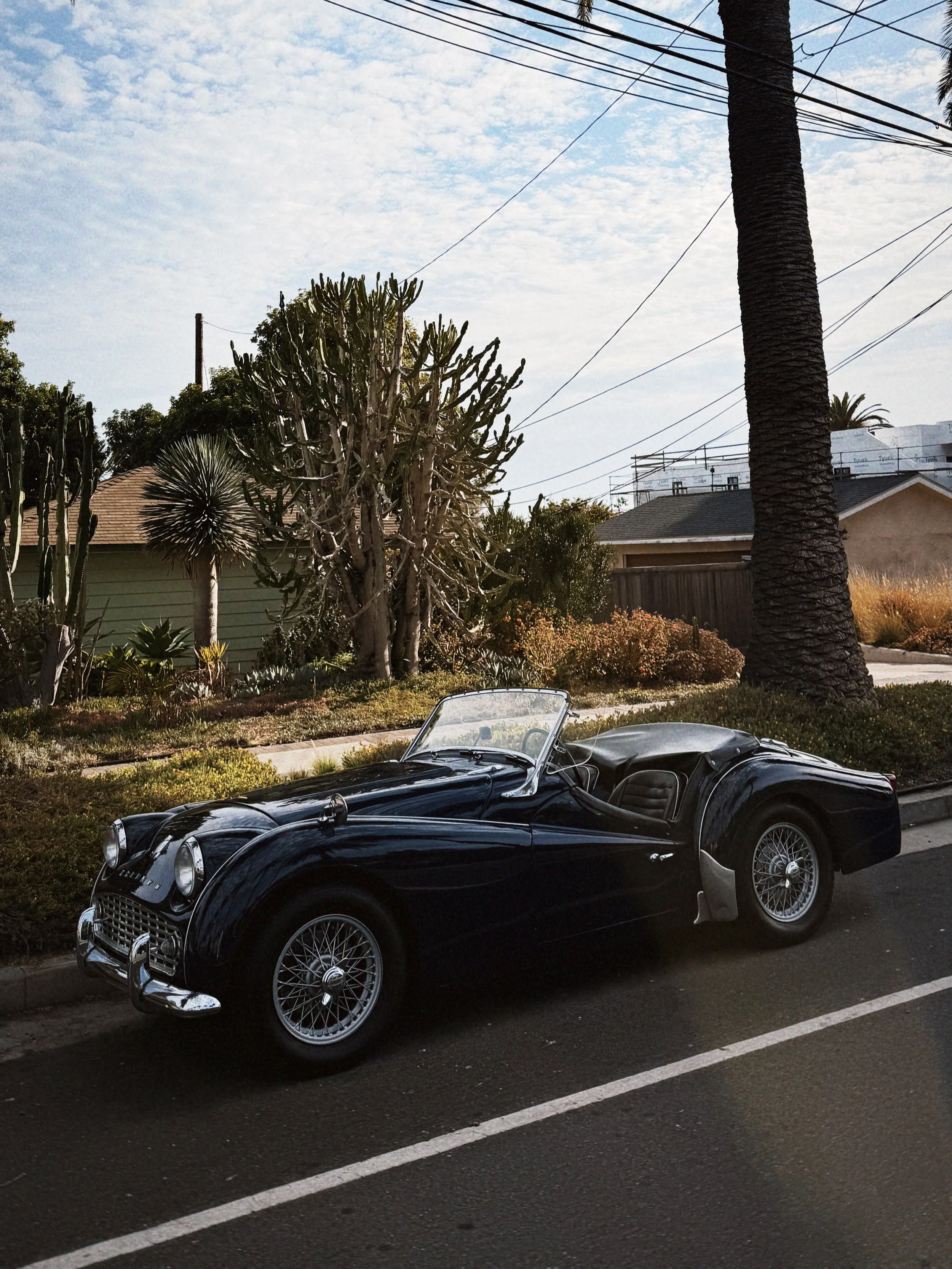 A black vintage convertible sports car parked on the street with trees and houses in the background