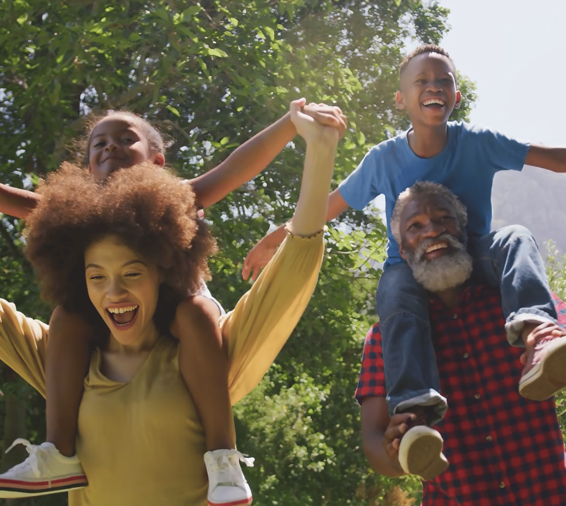 Family of four enjoying an outdoor activity, climbing on each other's shoulders in a green park, smiling and holding hands.