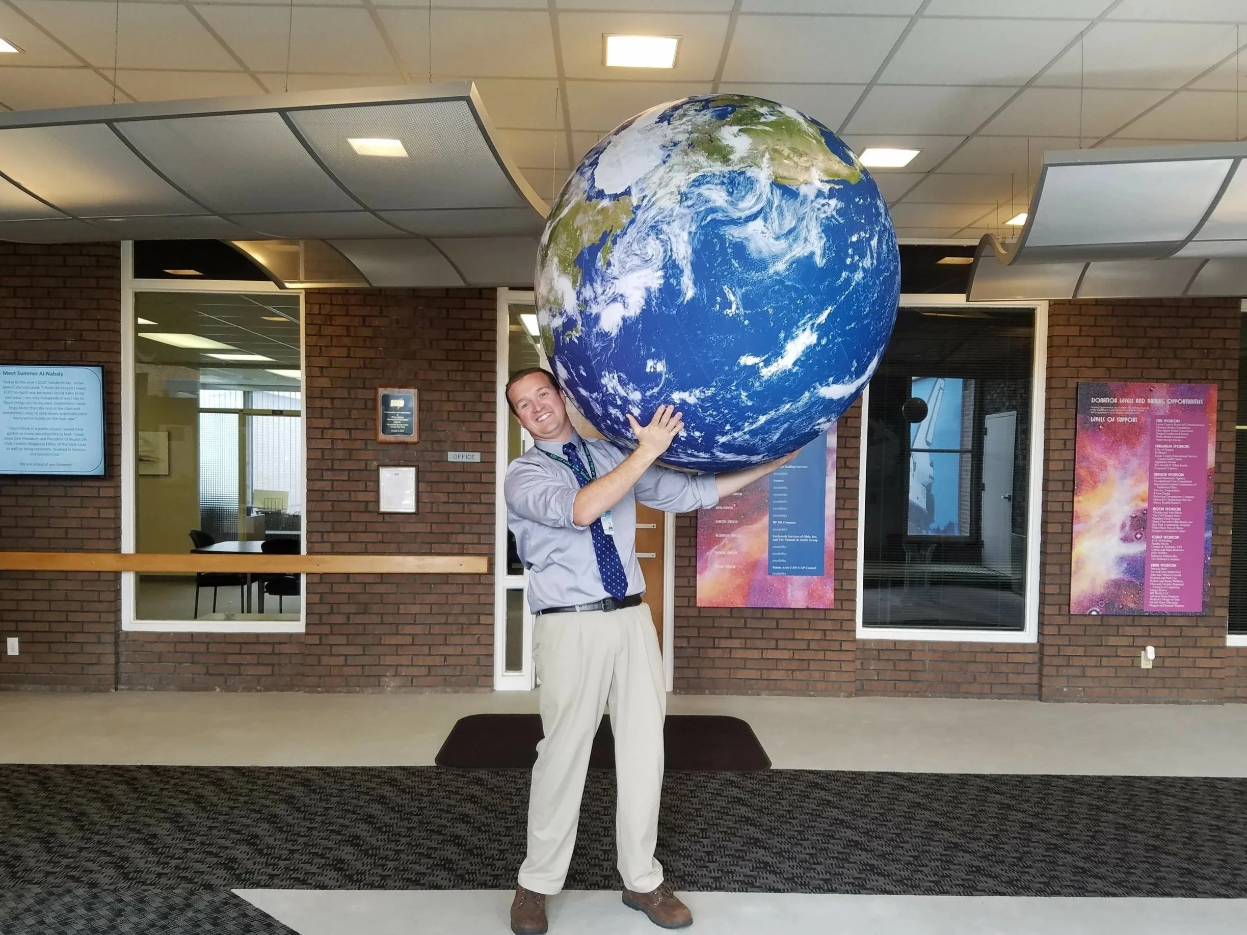 Dr. O'Brien is standing indoors holding a large inflatable globe of the Earth.