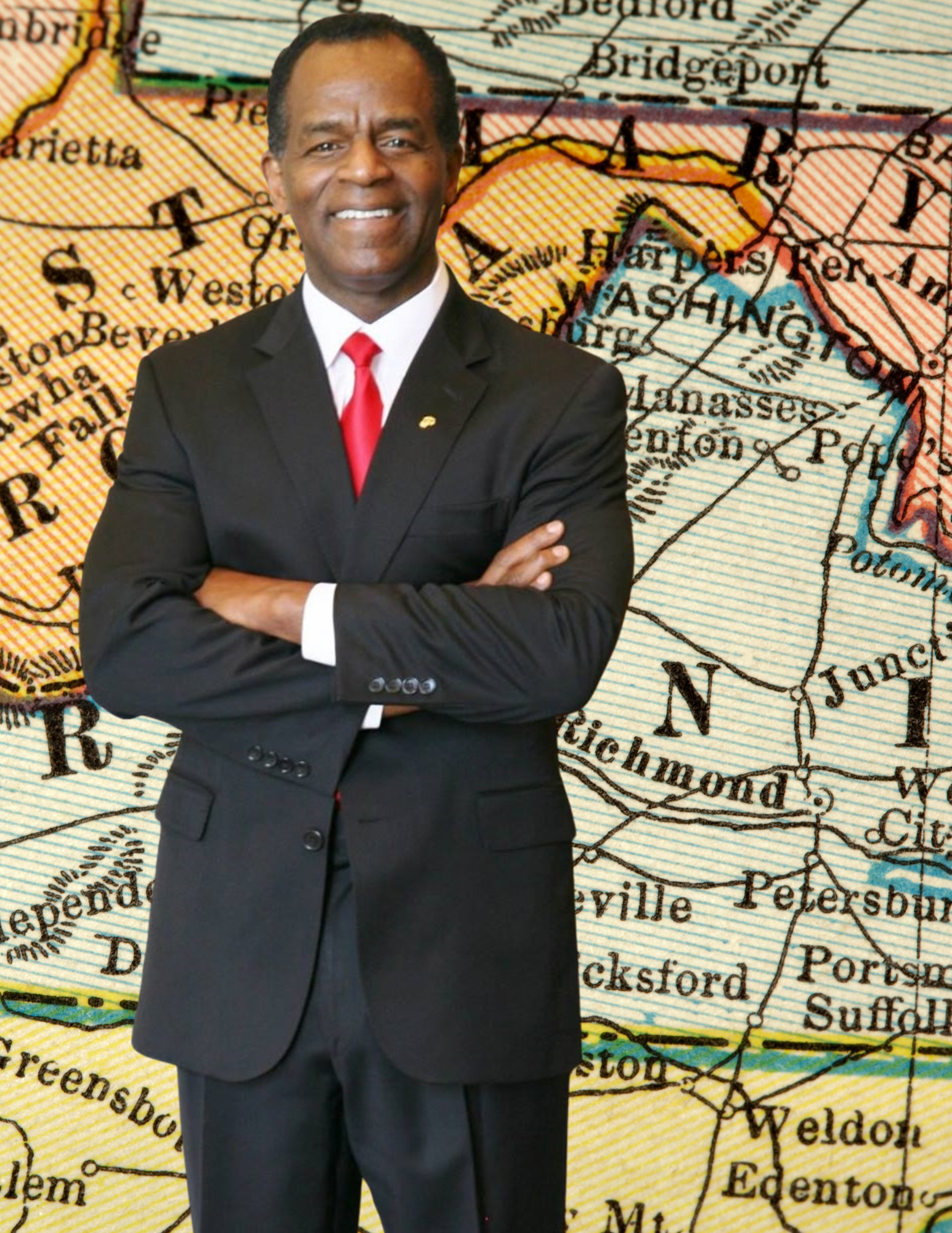 A man in a black suit with a white shirt and red tie standing with arms crossed, smiling, in front of a map highlighting Washington and surrounding areas.