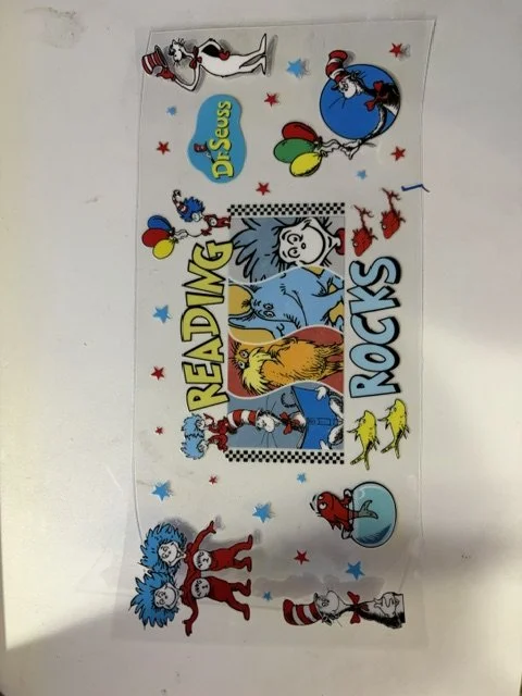 Decorative strip with characters from Dr. Seuss's 'The Cat in the Hat,' including the cat, the fish, the children, and other characters, surrounded by stars and balloons, with the text 'Reading Rocks.'