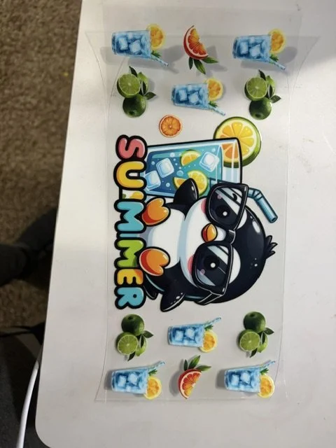 Colorful cartoon image of a black penguin wearing sunglasses holding a drink with ice and lemon, with the word 'SUMMER' in multicolored letters, surrounded by miniature drinks, lime, and grapefruit slices on a white background.