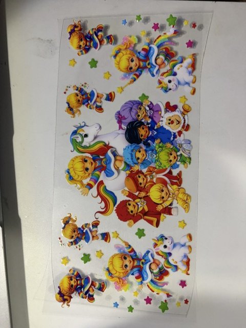 Colorful sticker sheet featuring characters dressed in rainbow-themed outfits, unicorns, rainbows, and stars.