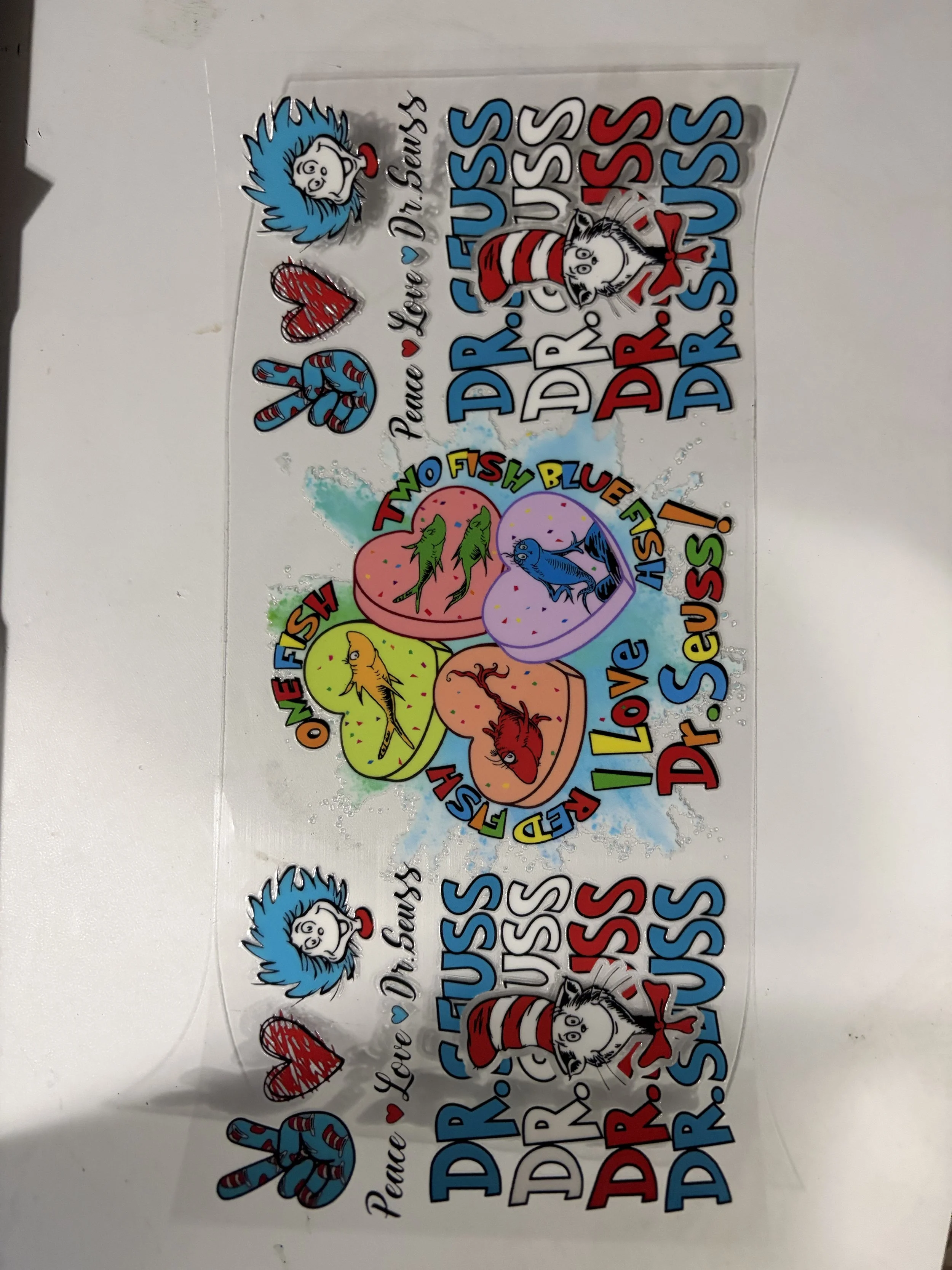 Colorful sticker sheet featuring Dr. Seuss characters and playful phrases. Includes illustrations of Thing 1 and Thing 2, the Cat in the Hat, and the Lorax. Phrases include 'Peace, love, you, Dr. Seuss' and 'Two fish blue fish' in multicolored letters.