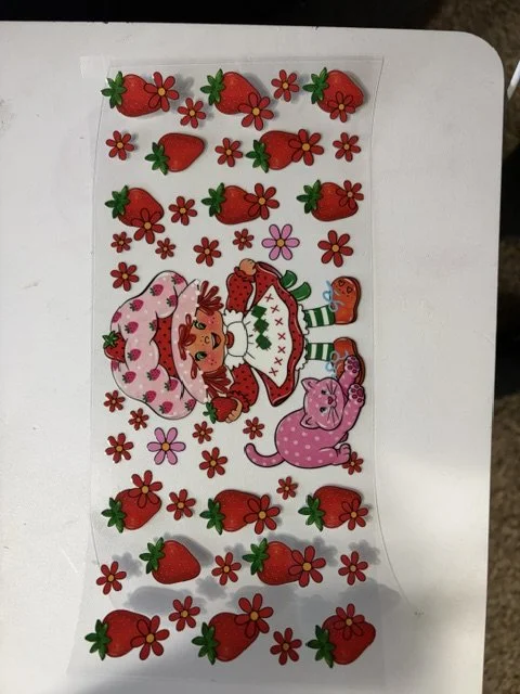 Sheet of decorative stickers featuring strawberries, red flowers, and a girl with red hair, a pink hat, and a pink puppy, all with colorful outfits and accessories.