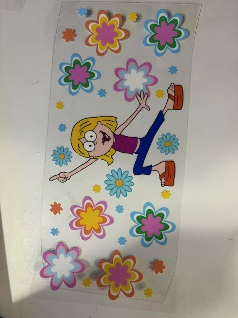 Colorful stickers of flowers and a cartoon girl with blonde hair, a purple shirt, blue pants, and orange shoes, lying on a flat surface.