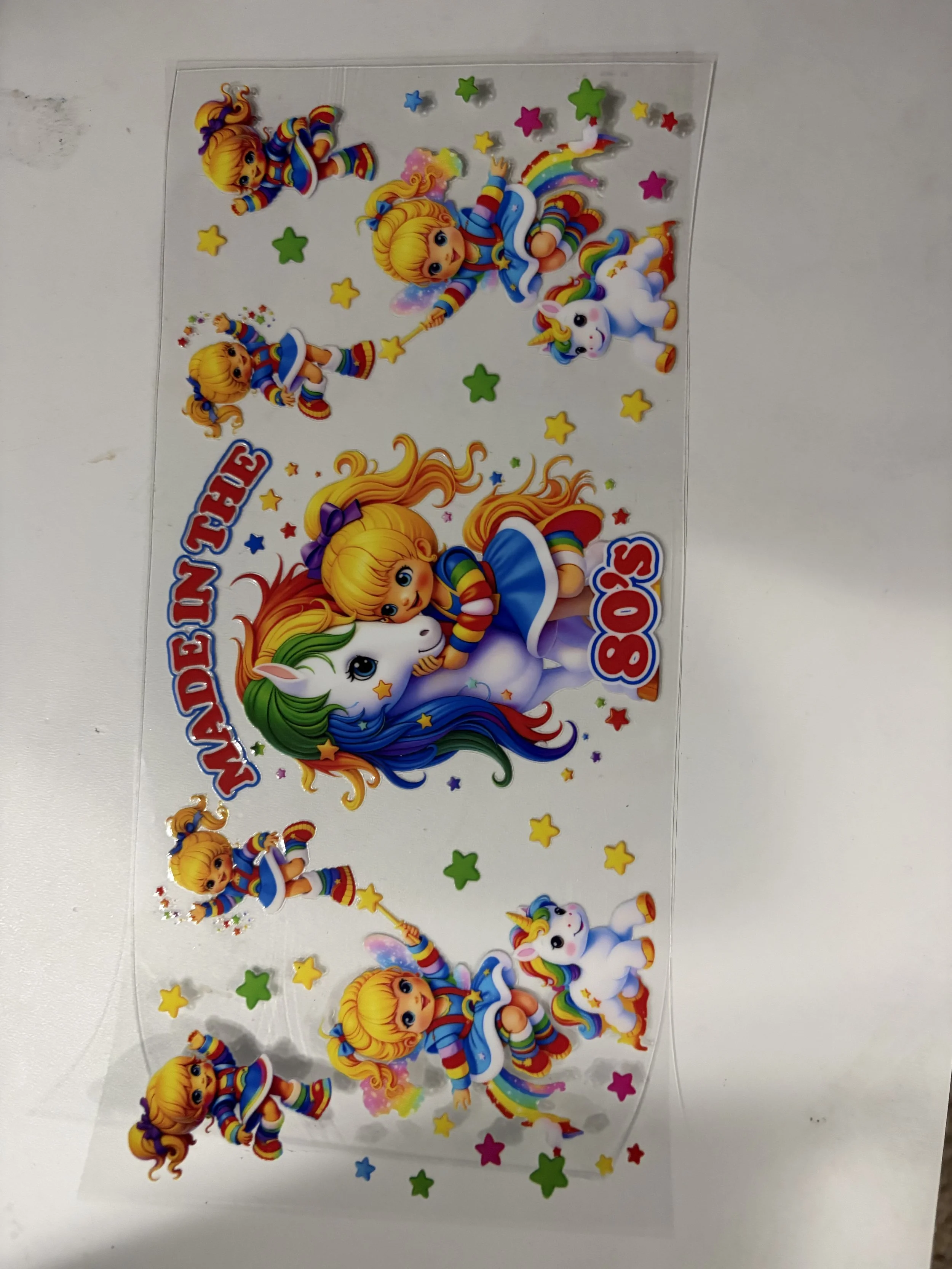 Colorful sticker sheet featuring cartoon unicorns, children in rainbow striped outfits, stars, rainbows, and the words 'MADE FREE' and '80'S'.